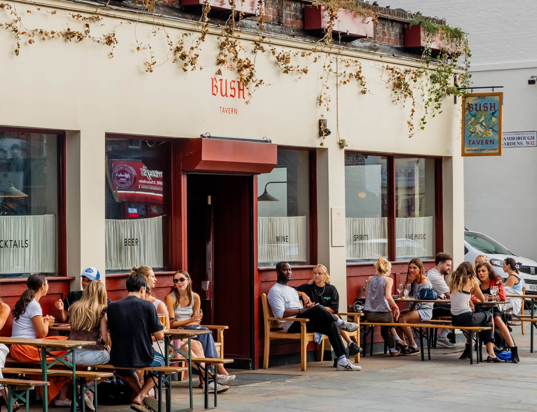 People drinking and eating outside the Bush Tavern in the sun bu the road