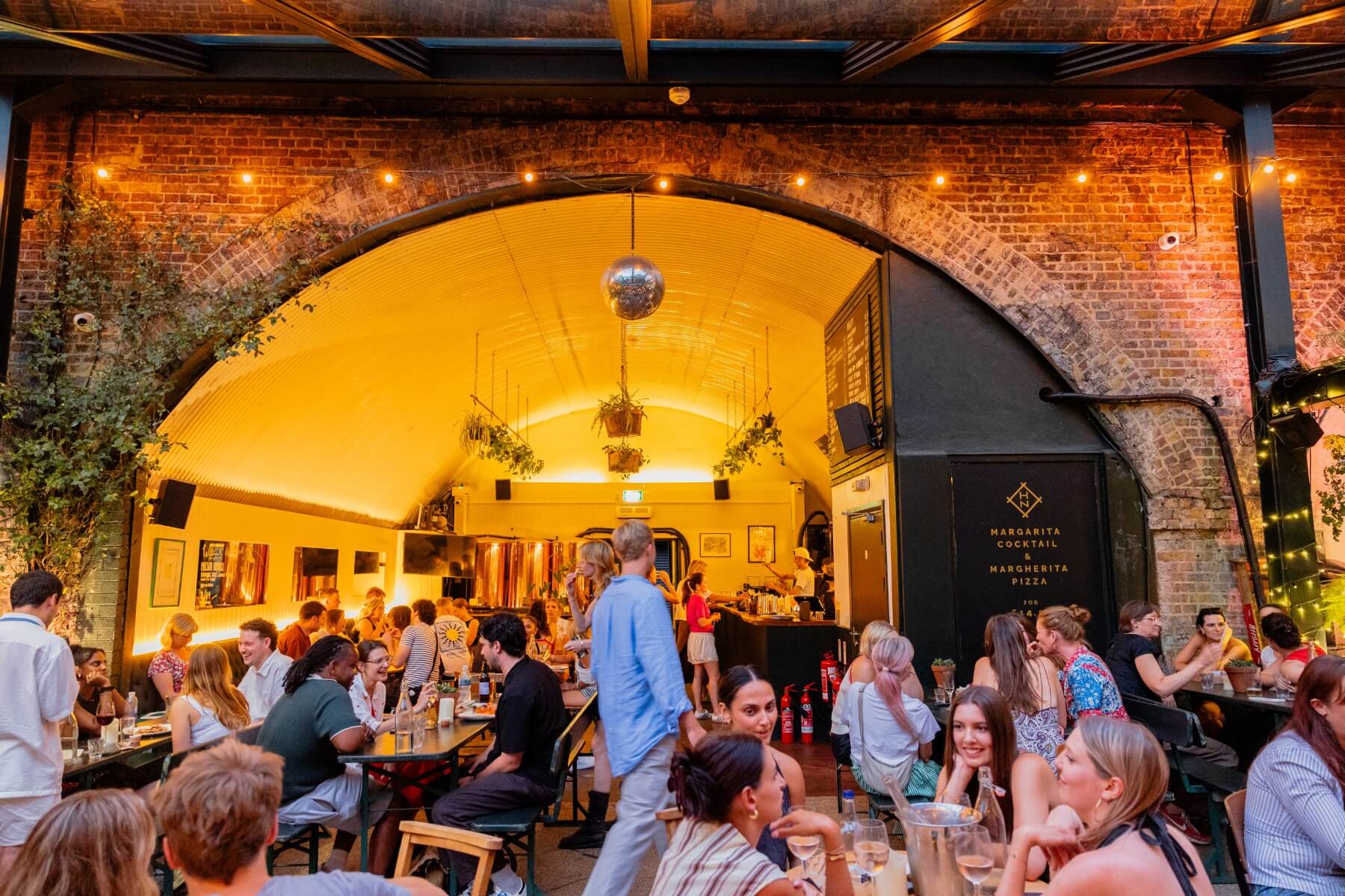 A warmly lit venue with flowers across the beams, atmospheric lighting and fairy lights